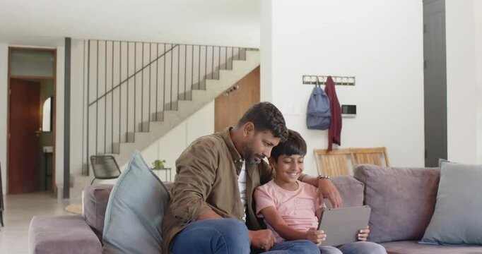 Indian father and son sitting on couch using tablet, bonding and learning together
