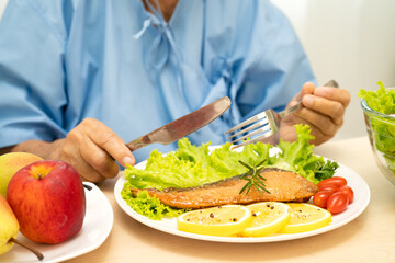 Asian elderly woman patient eating salmon steak breakfast with vegetable healthy food in hospital.