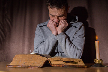 A European man reads an ancient book by candlelight.