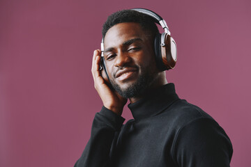Young African man enjoying music with headphones, wearing a black turtleneck, smiling with a purple background, showcasing a relaxed and positive vibe