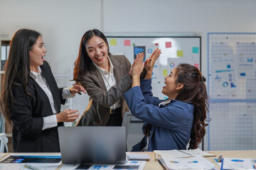 Three excited businesswomen are giving a high five to each other in the office, celebrating the success of their project, expressing joy and teamwork