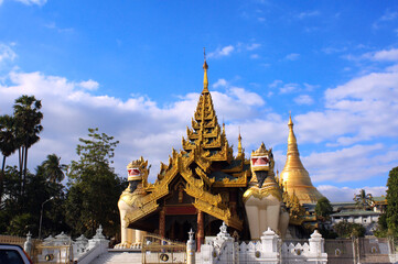 Fototapeta premium Golden statue of lion guardian and golden stupa in ancient buddhist complex. Stone figures of mythical creatures near to buddhist temple, Yangon, Myanmar (Burma)