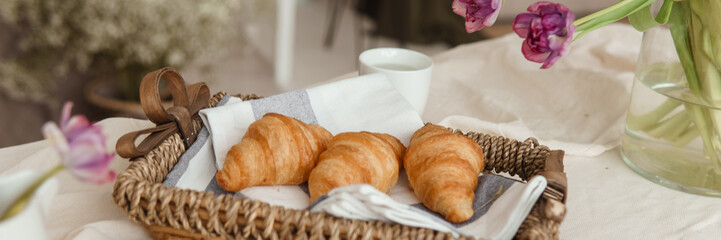 Fresh croissants in a wicker basket on the table next to a vase of lilac tulips.