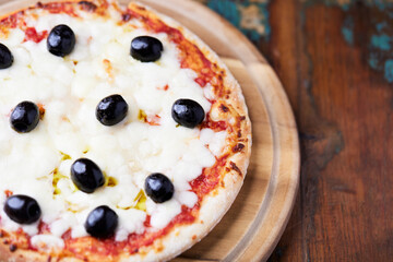 Pizza with mozzarella cheese and black olives on wooden background. Soft focus. Close up