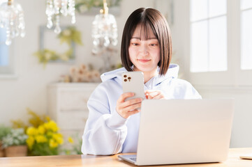 リビングでスマートフォンとノートパソコンを使う若い日本人女性
