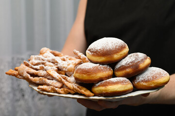 Świeżo usmażone pączki i faworki posypane cukrem oudrem na talerzu z bliska