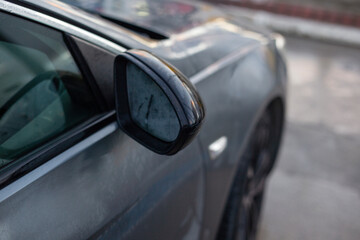 Close-up of a wet side mirror on a grey car, rearview mirror covered in morning dew