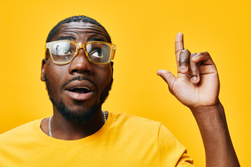 Portrait of a joyous young man with glasses wearing a yellow shirt against a vibrant yellow...