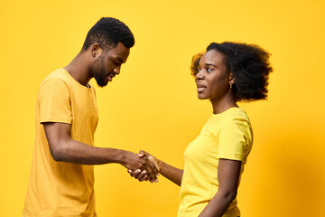 Obraz premium Young African couple shaking hands in matching yellow attire against a vibrant yellow background, symbolizing unity and collaboration in friendship or business