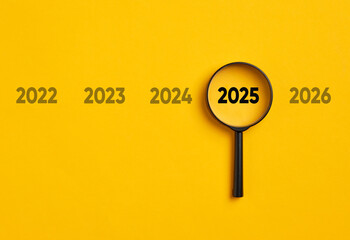 Magnifying glass focusing on year 2025 among other years on yellow background