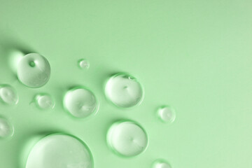 Glycerin gel texture. Transparent serum drop on green background with space for text. Liquid gel moisturizer with bubbles macro