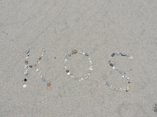 Aus Kieselsteinen gelegter Schriftzug Kos im feinen Sand am Strand von Kos