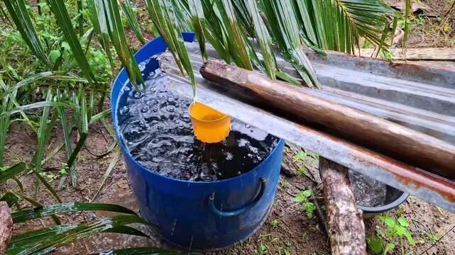A blue rainwater reservoir with a yellow dipper, the water flows from a zinc plate installed to transmit rainwater