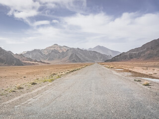 Asphalt road of the Pamir Highway in the valley of the Tien Shan Mountains in Tajikistan in the Pamirs, landscape in the high desert mountains for background, the road goes into the distance
