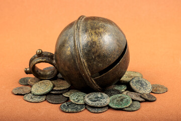 Ancient bronze bell with Roman coins on an orange background.