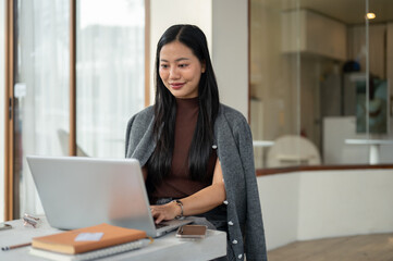 A beautiful Asian woman working remotely from a coffee shop in the morning, working on her laptop.