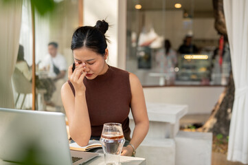 A frustrated Asian woman feels stressed while working, seated in front of her laptop.