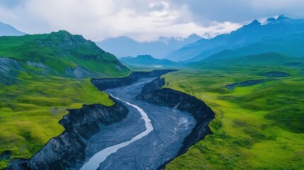 Fototapeta premium Lush green landscapes surround a winding river, framed by majestic mountains under a cloudy sky, showcasing the beauty of nature.