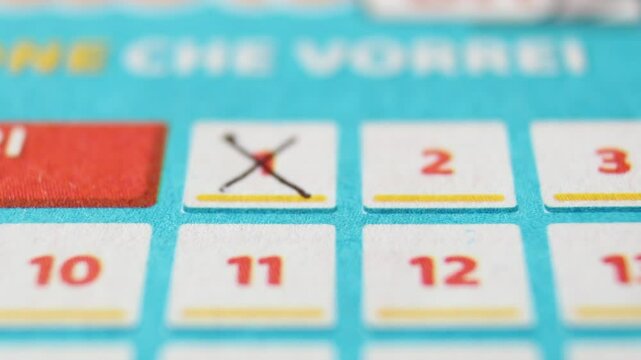 A man marks with a pen numbers 1, 13, 9, 31, 39 on a lottery ticket. The rows of red numbers in white squares on the blue ticket are arranged horizontally. Close-up horizontal video