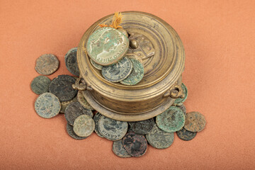 Ancient Roman coins scattered around a bronze inkwell on an orange background. © Edu Estellez