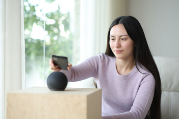 Asian woman pairing phone with smart speaker