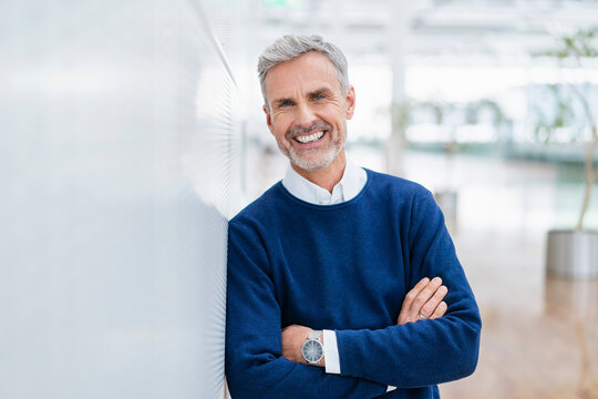 Smiling gray haired businessman with arms crossed leaning on wall
