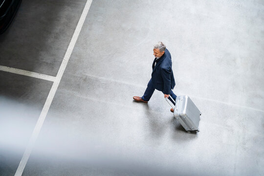 Mature businessman walking with suitcase in parking lot