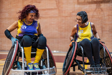 Happy women sitting on wheelchair and playing rugby at sports center