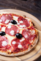 Pizza with salami and mozzarella cheese. Wooden background. Soft focus. Close up.