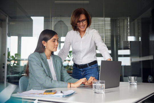Senior woman guiding co worker and using laptop at office