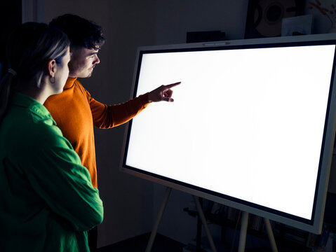 Man pointing at digital screen near woman in office
