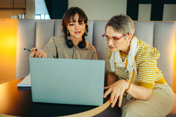 Colleagues collaborating across diverse ages using a laptop in a modern office setting,...