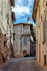 Medieval architecture and narrow streets of Assisi, traditional stone houses with balconies and a charming vintage scooter hidden in the distance.