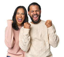 Young Latino couple in studio cheering carefree and excited. Victory concept.
