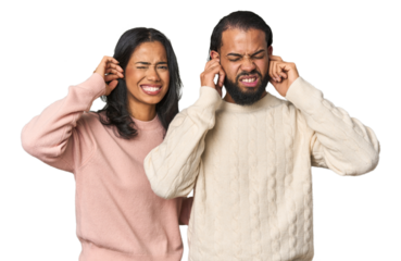 Young Latino couple in studio covering ears with fingers, stressed and desperate by a loudly ambient.