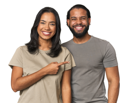 Young Latino couple in studio smiling and pointing aside, showing something at blank space.