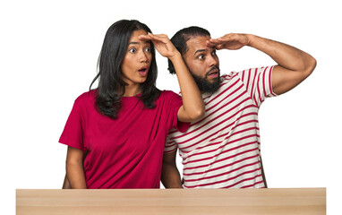 Seated young Latino couple at table looking far away keeping hand on forehead.