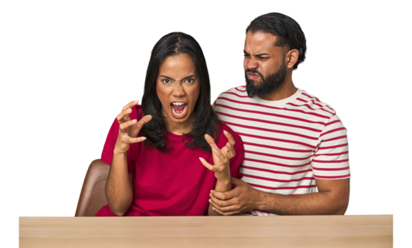 Seated young Latino couple at table screaming with rage.