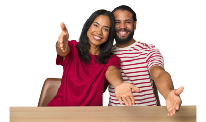 Seated young Latino couple at table showing a welcome expression.