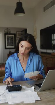 Young woman sit at table in living room calculates household utility bills, manage family budget, analyze personal finances, review expenses, incomes and outcomes working looks focused, vertical view