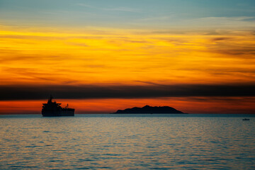 Sunset over the sea with an island and a container ship in the backlight