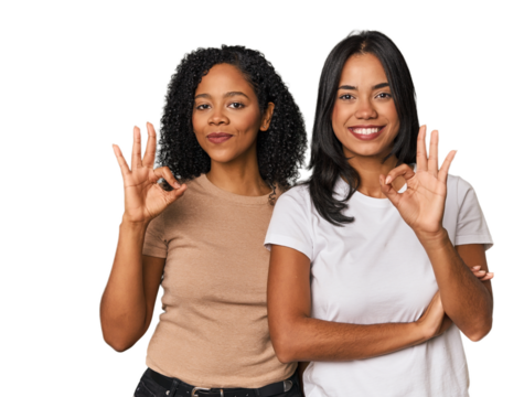 Young Latin friends in studio winks an eye and holds an okay gesture with hand.