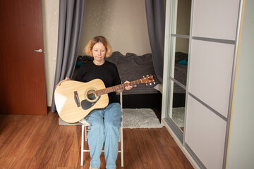 Woman playing acoustic guitar at home, music student studying chord structure, focused on rock and...