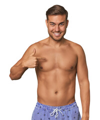 Fototapeta premium Young man shirtless in swimwear, studio person pointing by hand to a shirt copy space, proud and confident
