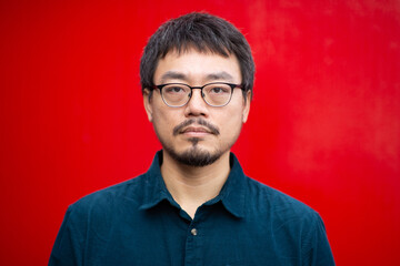 Obraz premium Portrait of an Asian man with glasses on a red background