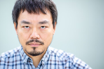Obraz premium Serious Asian man with intense gaze in a checkered shirt against a plain background