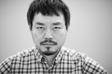 Obraz premium Black and white portrait of a serious Asian man in a checkered shirt