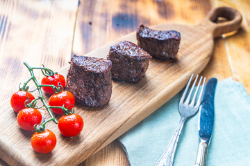 Filet mignon, beef steaks on a wooden board with cherry tomatoes with a napkin and cutlery on the table. High quality photo