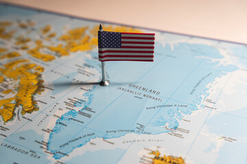 An American flag pin placed on Greenland on a world map, highlighting the geopolitical relationship and potential US interests in the Arctic region © Rokas
