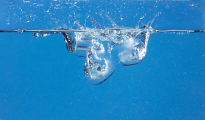 Falling ice tube in motion with splashing water, creating air bubbles scatter around, blue...